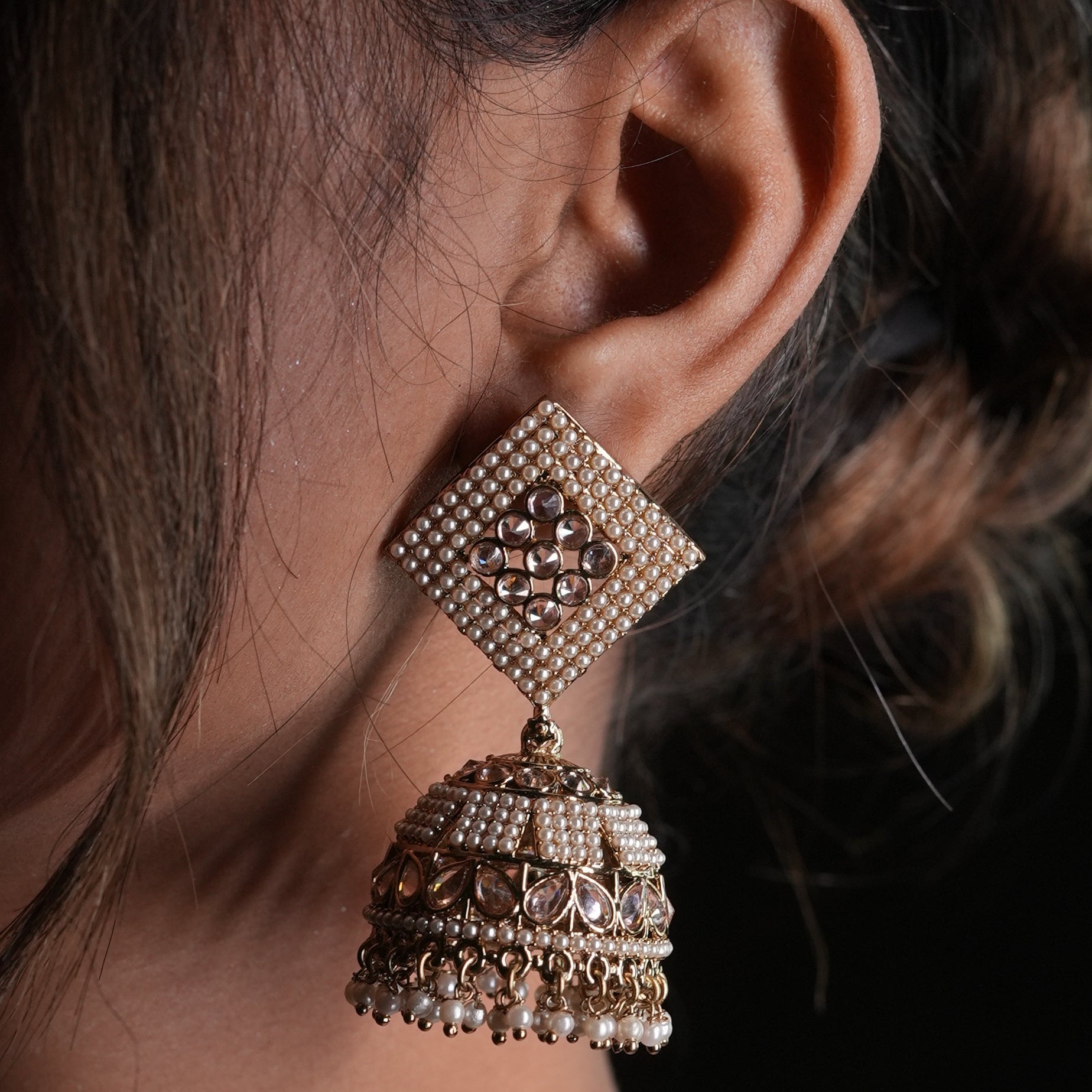 Close-up of a person wearing ornate gold earrings with a blurred background