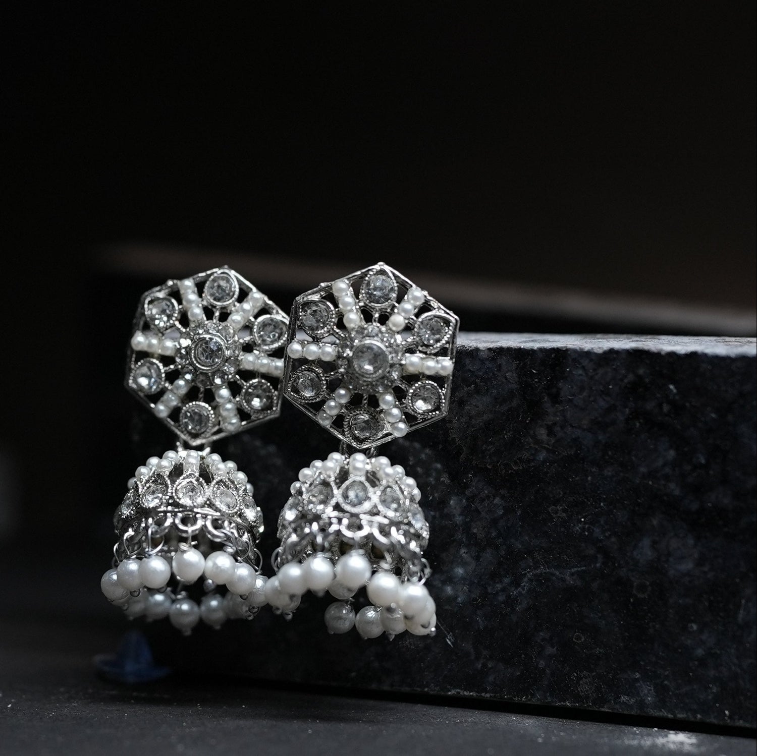 Pair of silver earrings with pearl accents on a dark background